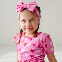 Image of a child wearing a Pink XOXO luxe bow headband and matching short sleeve two piece pajama set