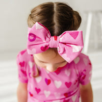 Close up image of a child wearing a Pink XOXO luxe bow headband and matching short sleeve two piece pajama set