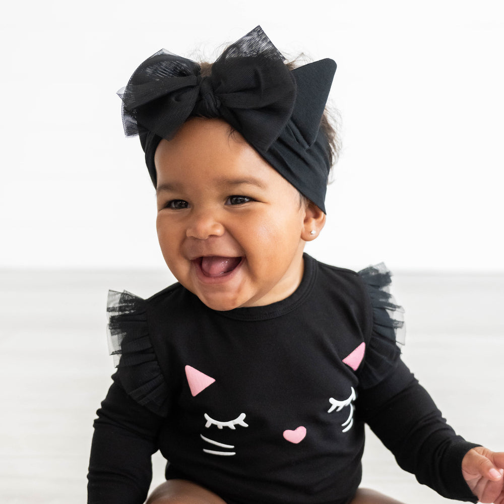 Baby smiling while wearing the Cat Ears Luxe Bow Headband and Black Cat Graphic Flutter Bodysuit