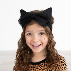 close up image of a child wearing a Classic leopard print pj set and a black cat ears luxe bow headband