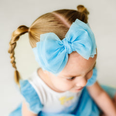 Close up image of a child wearing a Blue tulle luxe bow headband and coordinating Play dress
