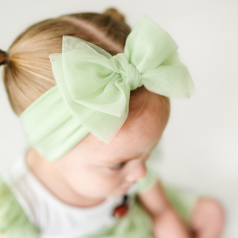 Close up image of a child wearing a Green tulle luxe bow headband