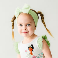 Close up image of a child wearing a Green tulle luxe bow headband and matching dress