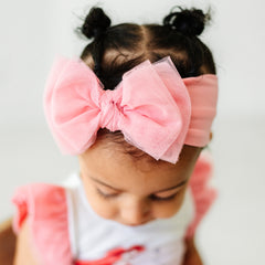 Close up image of a child wearing a Pink tulle luxe bow headband