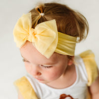 Close up image of a child wearing a Yellow tulle luxe bow headband
