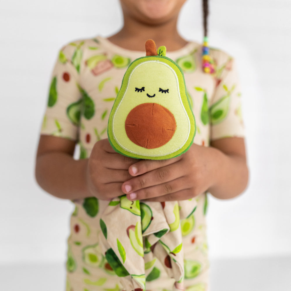 Close up image of a child holding up a Guac the Avocado sleepyhead lovey