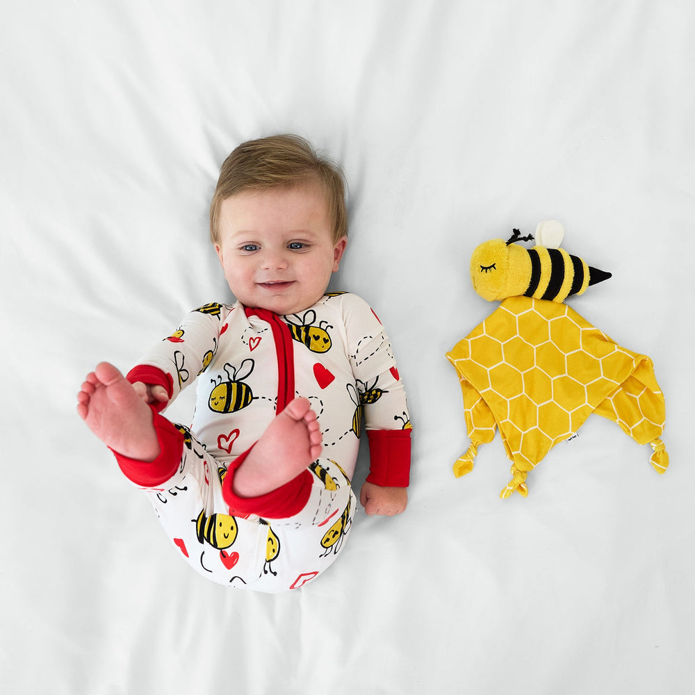 Image of a child laying on a bed next to  a Honey the Bumble Bee lovey 