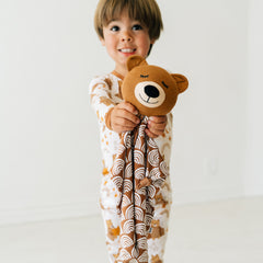 Child holding out a Bowie the Bear lovey wearing a Beary Sleepy two piece pajama set