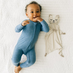 Child laying on a bed wearing a Heather Blue zippy next to a Clementine the Cat lovey