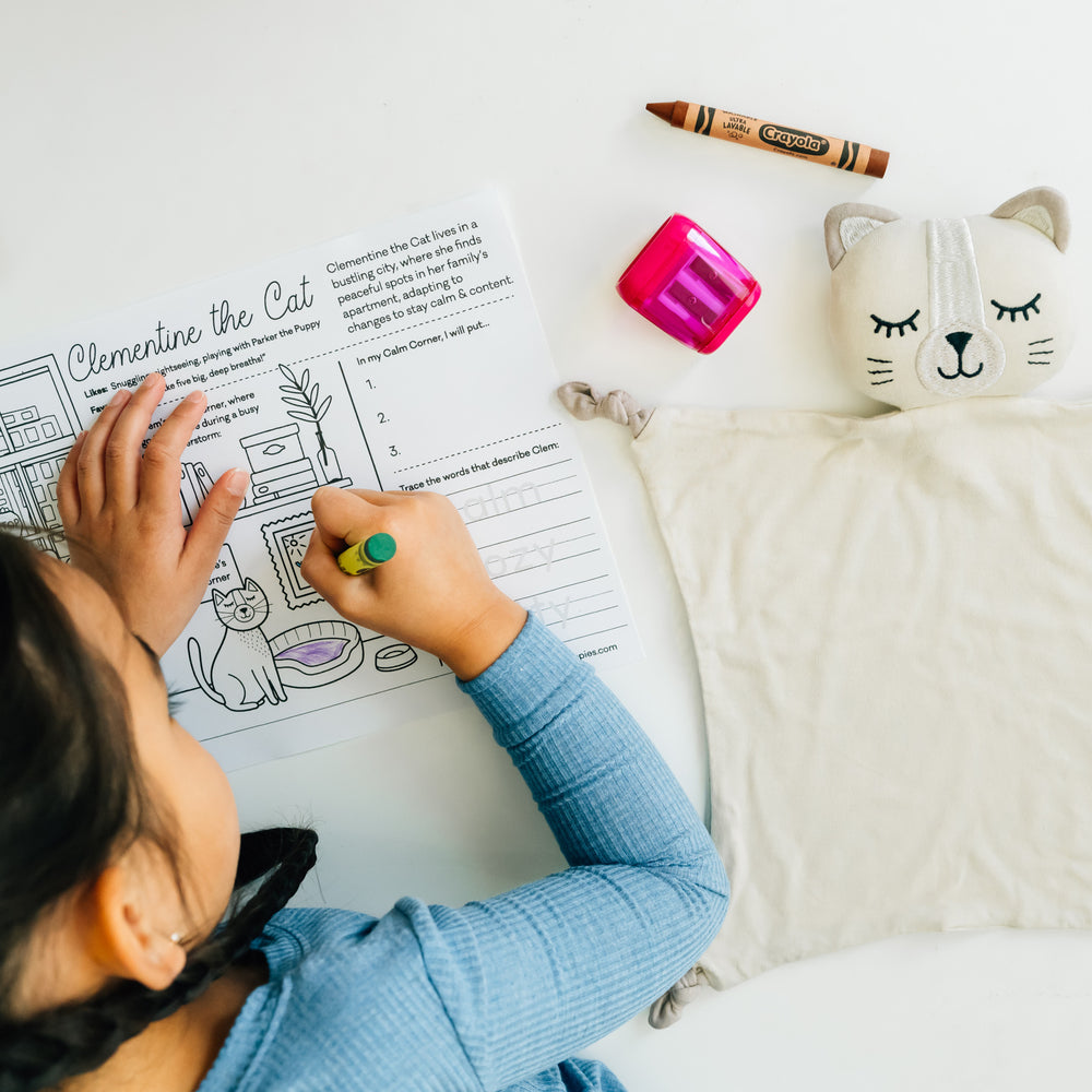 Child filling out a Clementine the Cat coloring page with her Clementine the Cat lovey