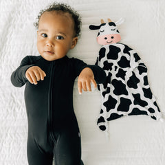 Child laying on a bed wearing a Black zippy next to his Charlie the Cow lovey