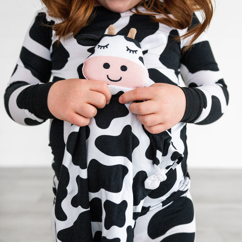 Close up image of a child holding a Charlie the Cow lovey wearing moo crew pjs