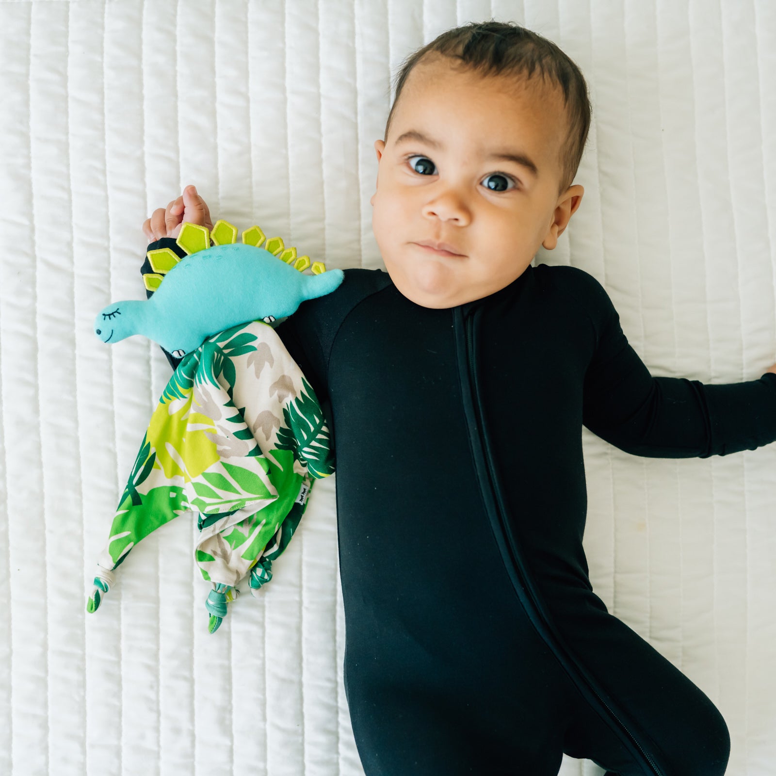child laying on a bed wearing a Black zippy with his Des the Dinosaur lovey