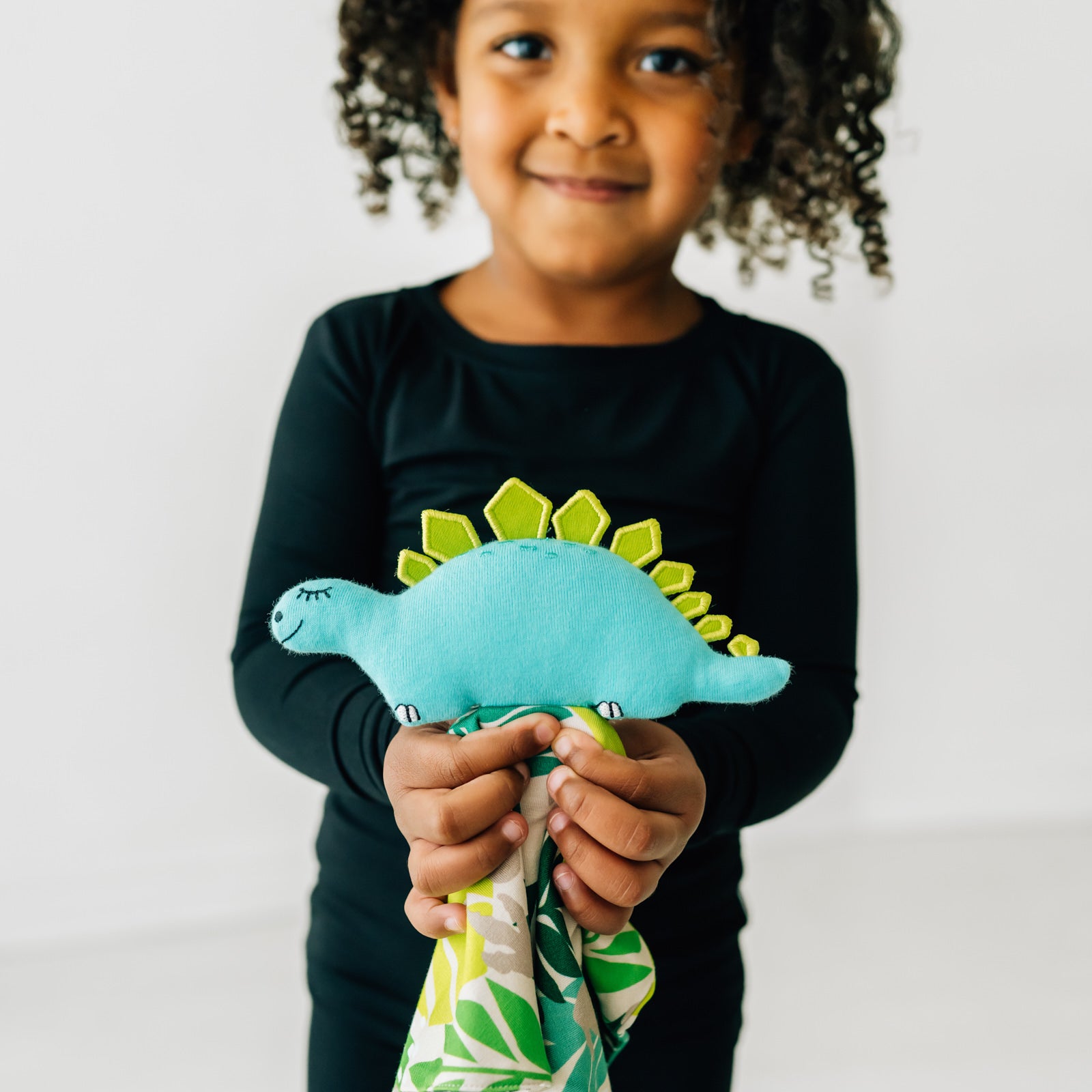 Close up image of a child holding out a Des the Dinosaur lovey