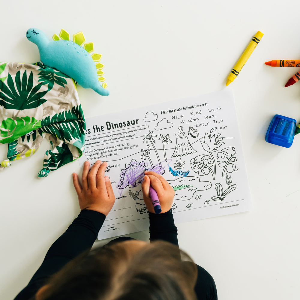 Child coloring in a Des the Dinosaur coloring page with their Des the Dinosaur lovey