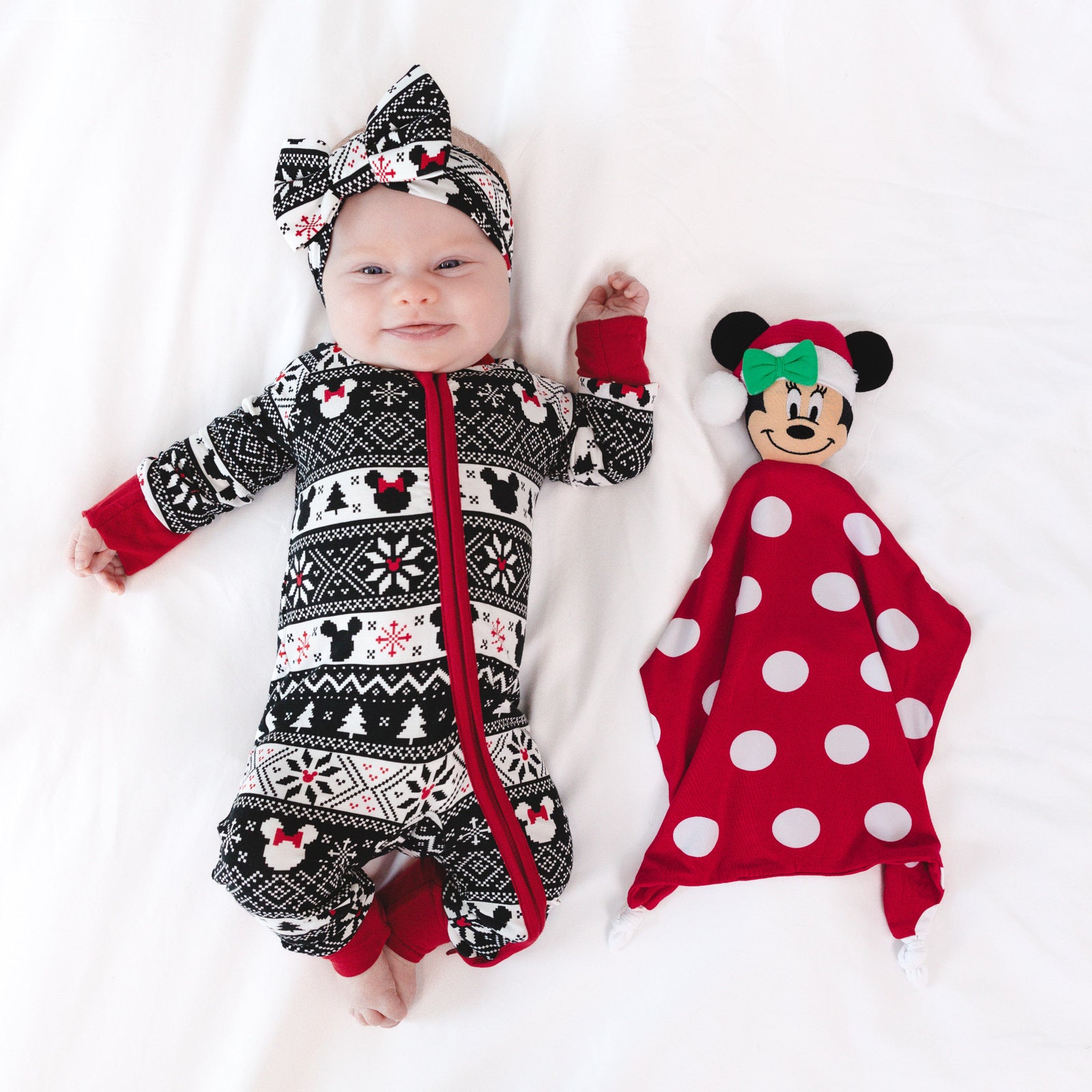 Child wearing a Mickey Fair Isle zippy and matching luxe bow headband next to a Minnie lovey