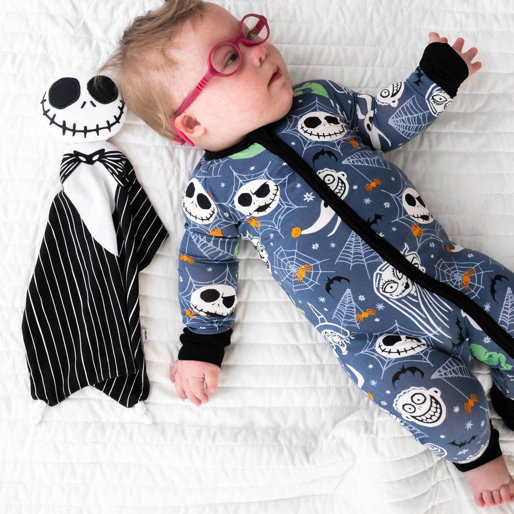 Top view image of baby laying down next to the Disney Jack Skellington Lovey, while wearing the Disney Jack & Crew Zippy