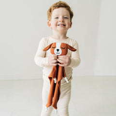 Child wearing a Heather Oatmeal two piece pj set holding a Parker the Puppy lovey