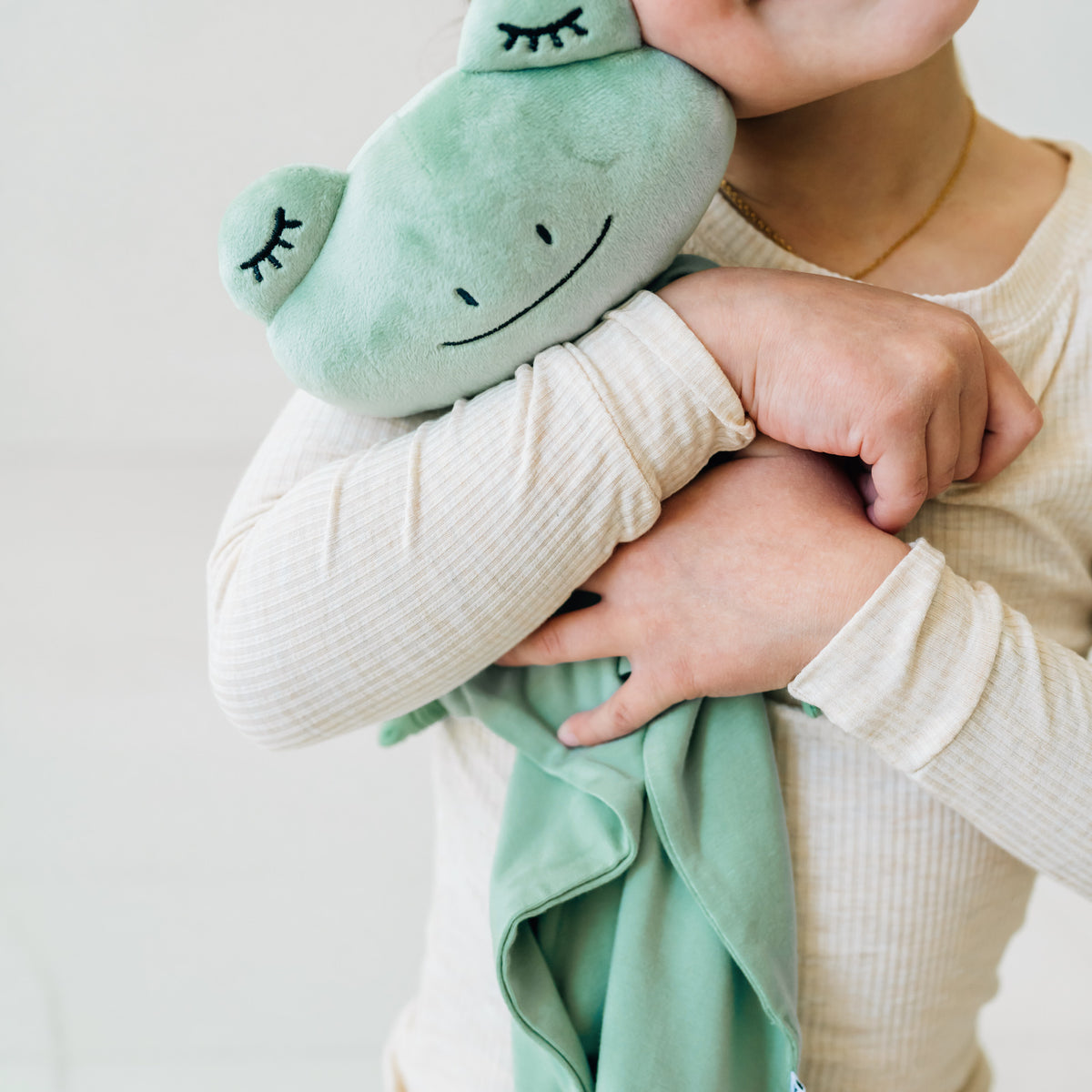 Close up image of a child cuddling their Fredrik the Frog lovey