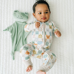 Child laying on a bed wearing a Check Mates zippy next to a Fredrik the Frog lovey