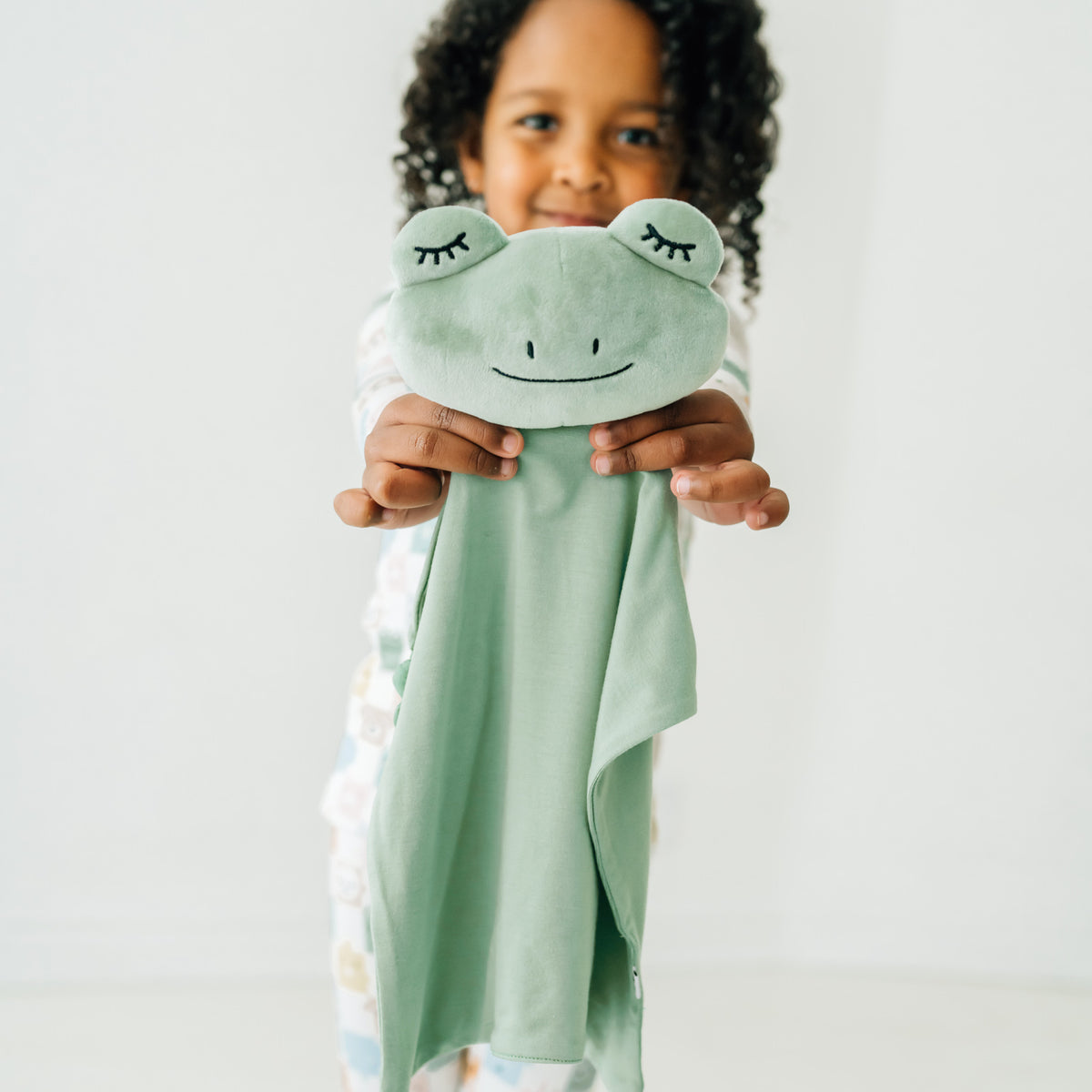 Child holding out a Fredrik the Frog sleepyhead lovey