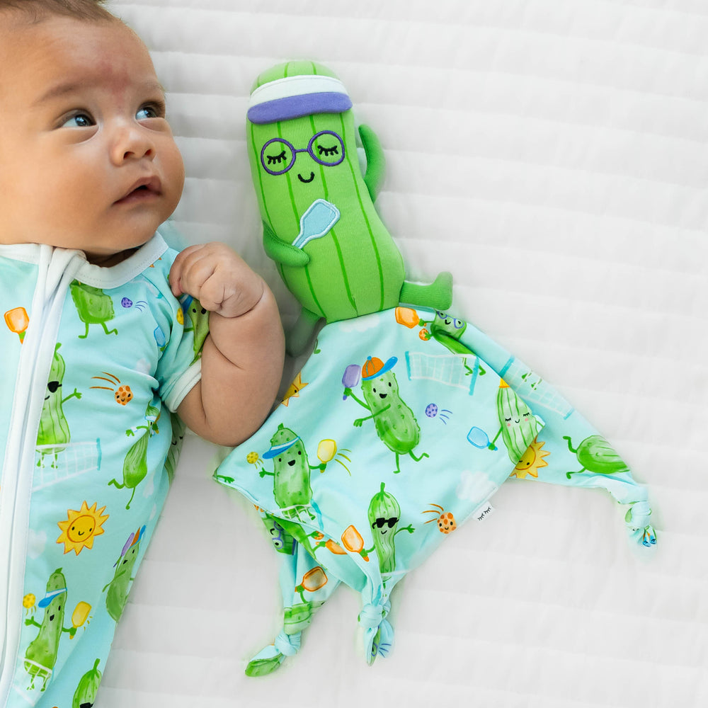 Baby laying down  wearing the Pickle Power Shorty Zippy, next to the Piper the Pickle Sleepyhead Lovey