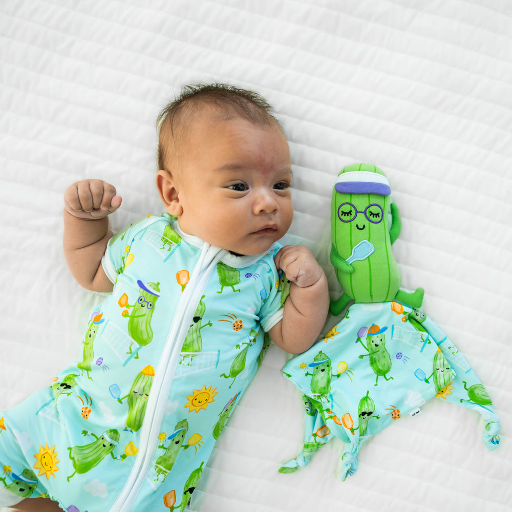 Alternative image of a baby laying down  wearing the Pickle Power Shorty Zippy, next to the Piper the Pickle Sleepyhead Lovey