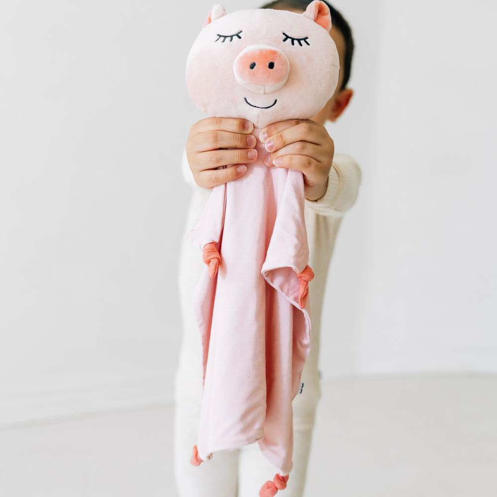 Alternate close up image of a child holding up a Pennie the Pig lovey