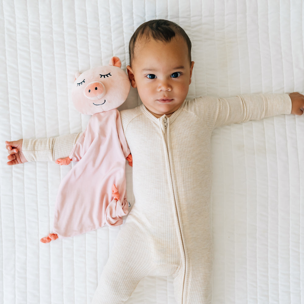 Child wearing a Heather Oatmeal zippy with their Pennie the Pig lovey