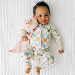 Child laying on a bed wearing a Check Mates zippy holding a Pennie the Pig lovey