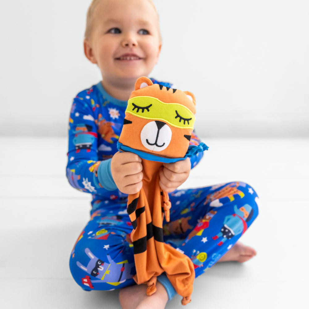 Child wearing the blue sleepy heroes two piece pj set holding the Tobey the Tiger lovey