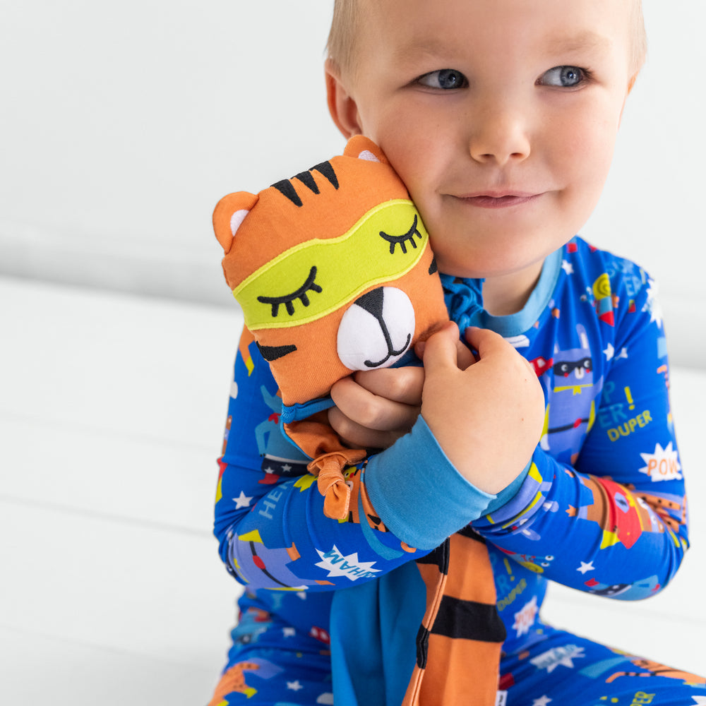 Child wearing the blue sleepy heroes two piece pj set hugging the Tobey the Tiger lovey