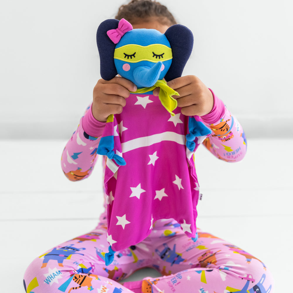 Child holding up an Ellie the Elephant lovey while wearing a pink sleepy heroes two-piece pajama set