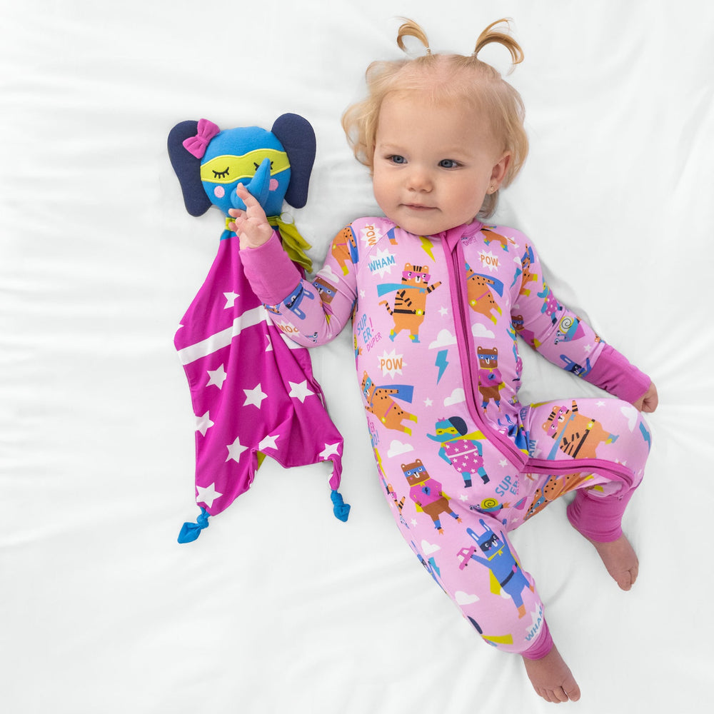 Child laying with an Ellie the Elephant lovey while wearing a pink sleepy heroes zippy