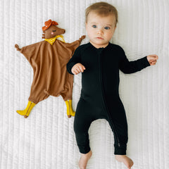 Child laying on a bed wearing a Black zippy with their Harley the Horse lovey