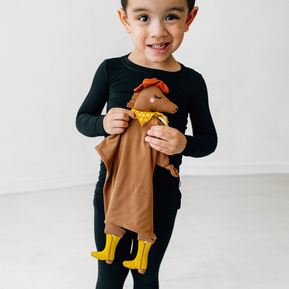Child wearing a Black two piece pj set holding his Harley the Horse lovey