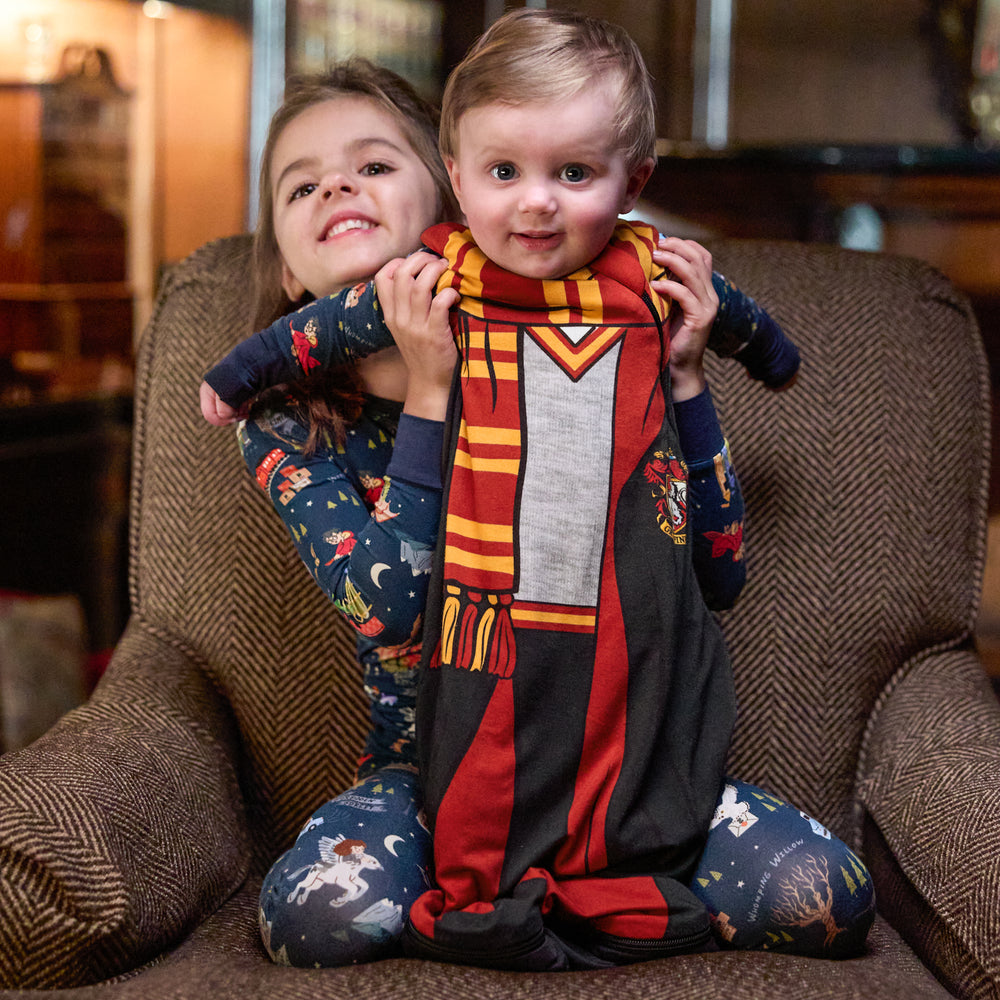 two children sitting on a chair. One child is holding up a child wearing a Gryffindor sleepy bag