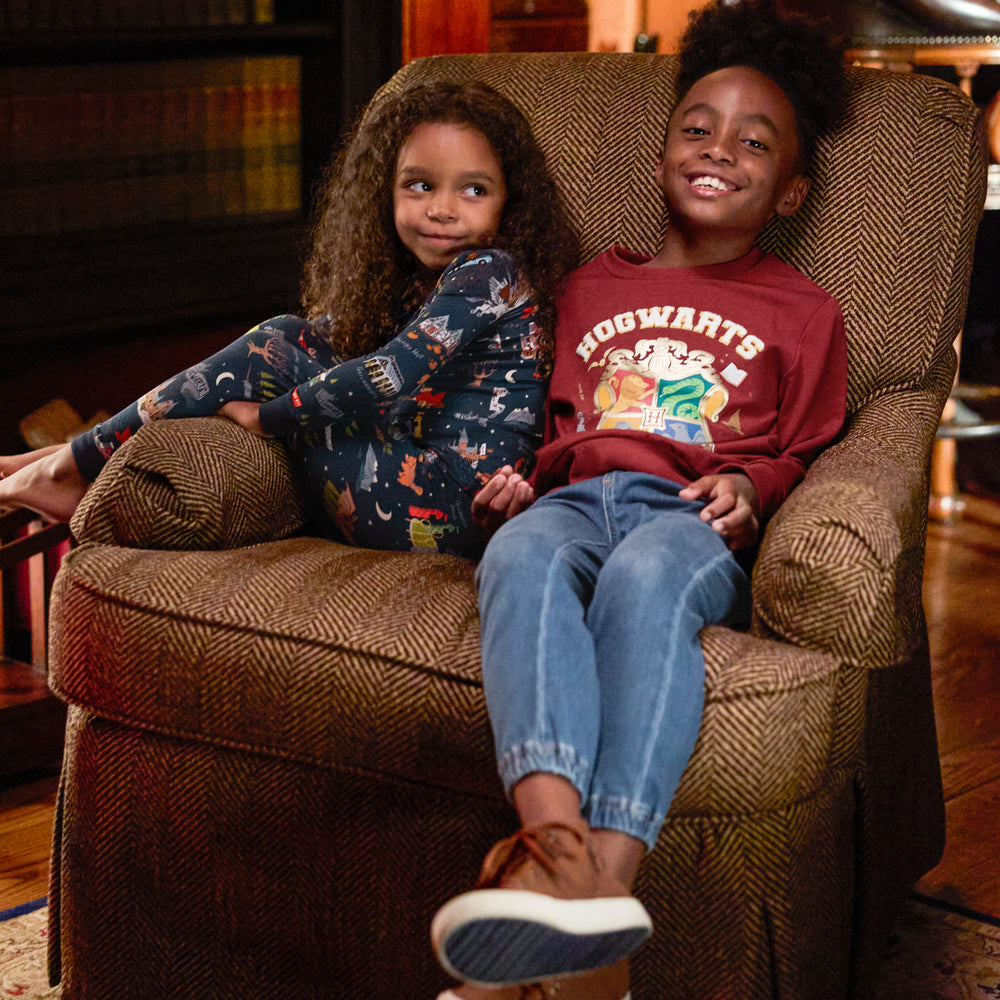 two children sitting in a chair wearing an Evening at Hogwarts two piece pj set and a Hogwarts crewneck sweatshirt and denim joggers