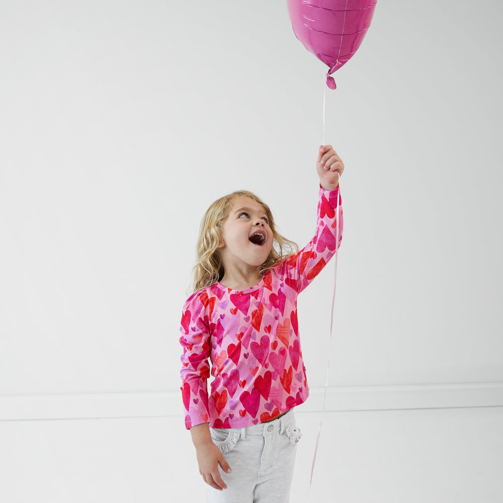 Child holding a pink balloon wearing a Pink Hearts & Crafts Puff Sleeve Tee and coordinating pants