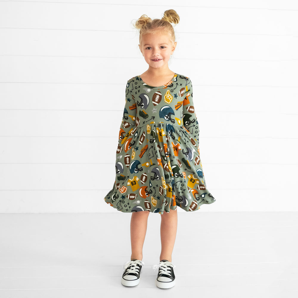 Image of a child wearing a Touchdown Time Twirl Dress with her hands in the pockets