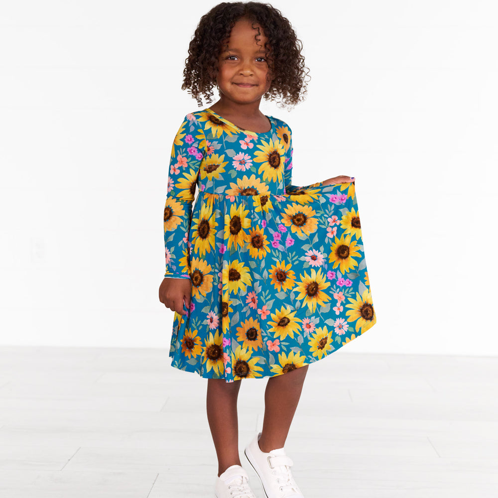 Image of a child wearing a Sunflower Fields Twirl Dress, holding up the side of the dress