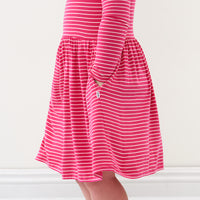 Close up image of a child wearing a Pink Punch Stripes bow back skater dress detailing the pocket