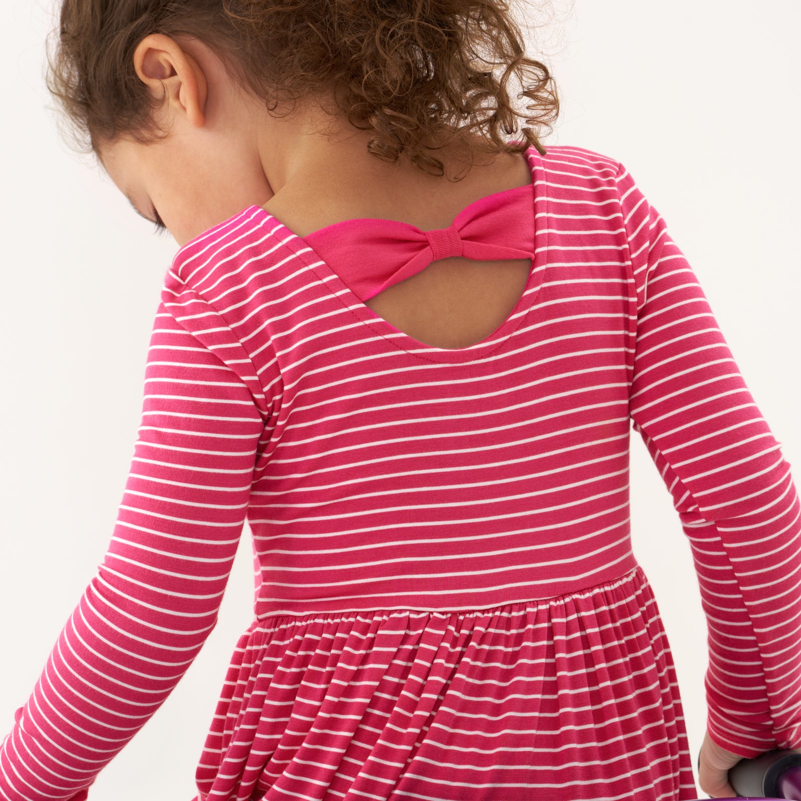 Back view image of a child wearing a Pink Punch Stripes bow back skater dress detailing the bow back