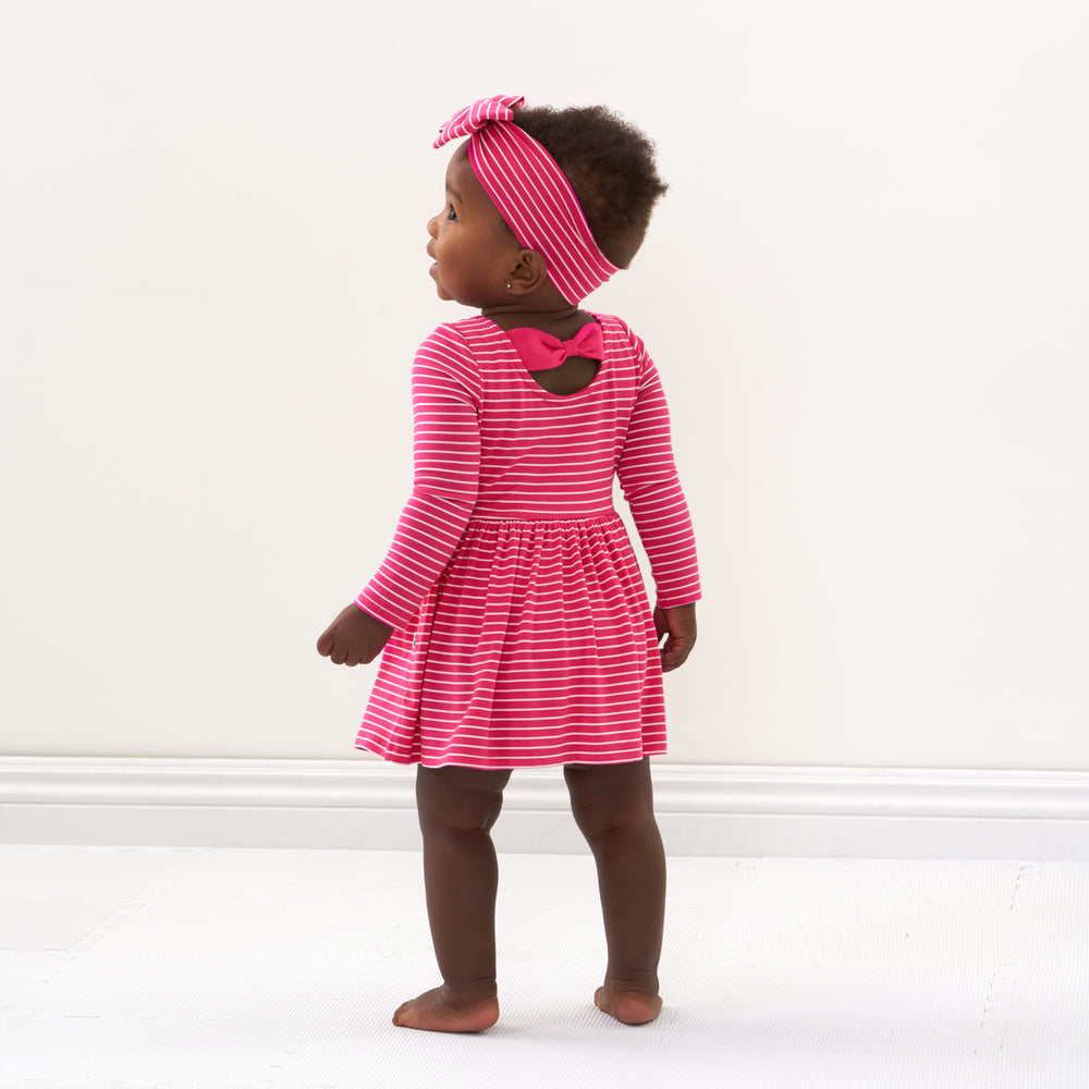 Click to see full screen - Back view image of a child wearing a Pink Punch Stripes bow back skater dress with bodysuit and matching Luxe Bow Headband