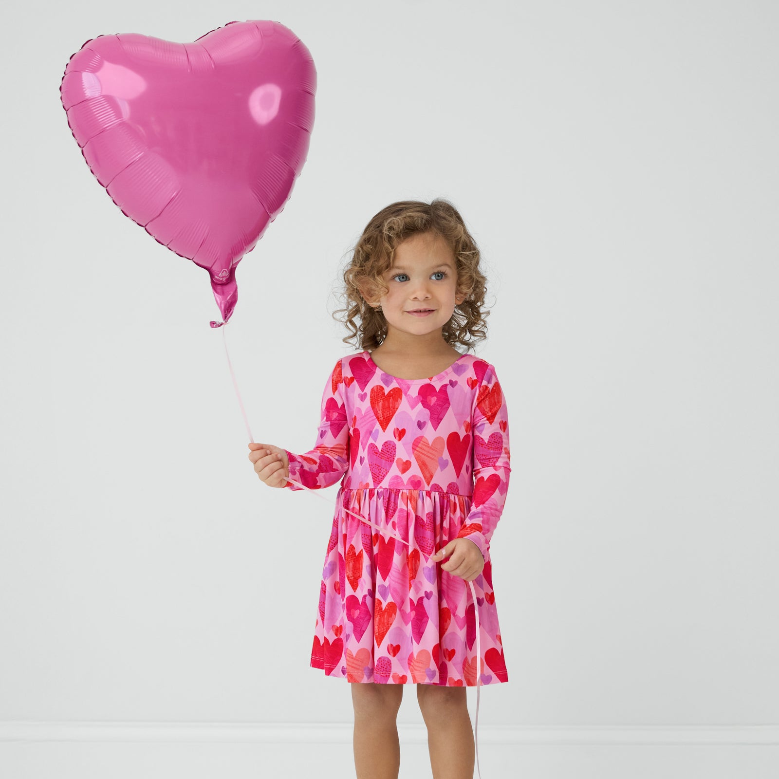 Child holding a pink heart balloon wearing a Pink Hearts & Crafts Bow Back Skater Dress with Bodysuit