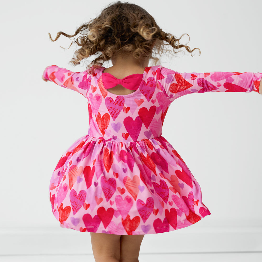 Back view of a child spinning around wearing a Pink Hearts & Crafts Bow Back Skater Dress with Bodysuit