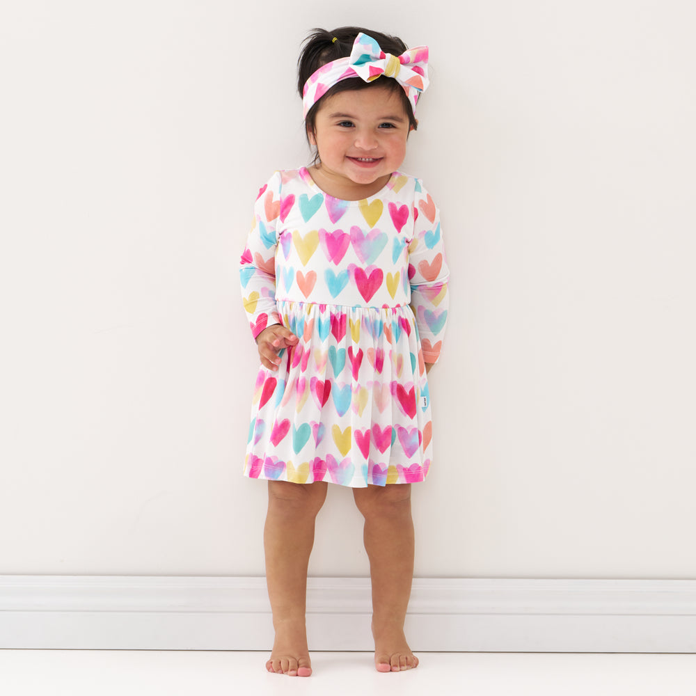 Click to see full screen - Child wearing a Watercolor Love bow back skater dress with bodysuit and matching luxe bow headband