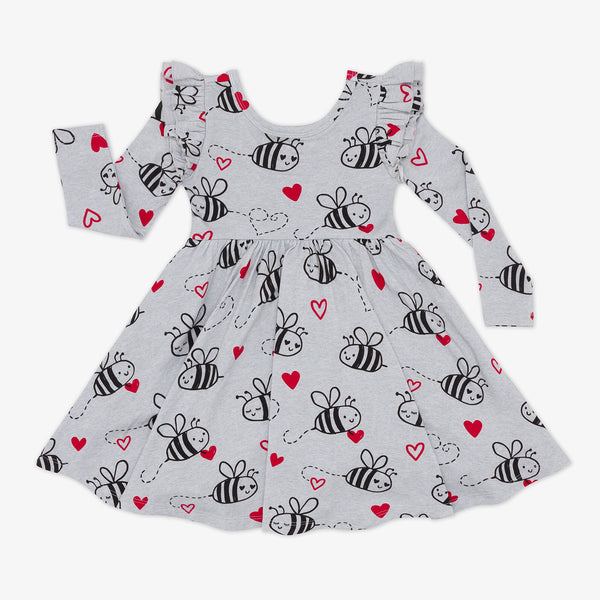 flat lay of a bee mine flutter twirl dress featuring black drawings of bees and red hearts on a gray background with ruffles at the shoulders