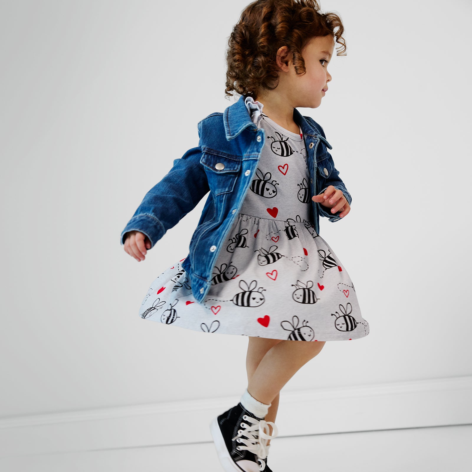 Child running wearing a bee mine flutter twirl dress with bodysuit and a midwash blue denim trucker jacket