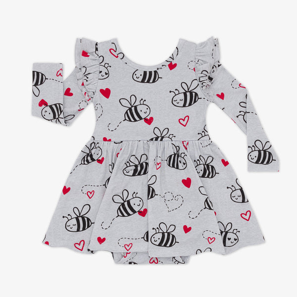 flat lay of a bee mine flutter twirl dress with bodysuit featuring black drawings of bees and red hearts on a gray background with ruffles at the shoulders